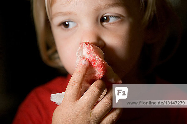 Junge hält blutbeflecktes Seidenpapier über die Nase