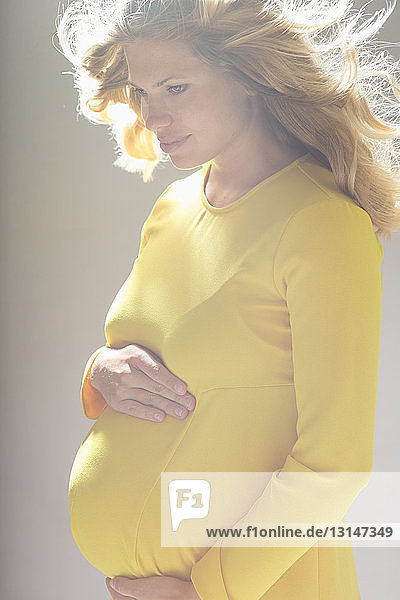 Studio portrait of pregnant young woman looking down whilst holding stomach