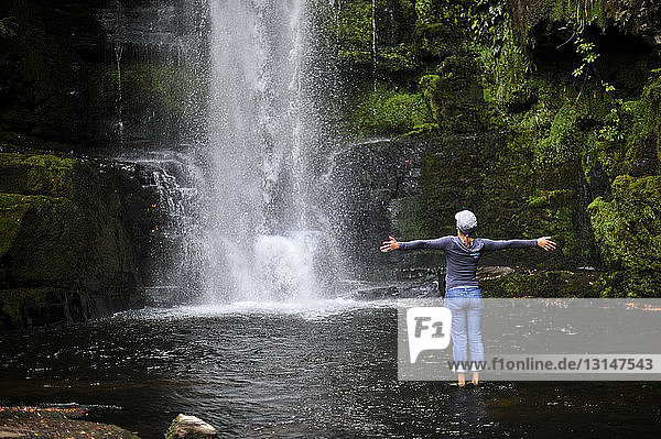 Frau steht mit ausgestreckten Armen am Wasserfall  Neuseeland