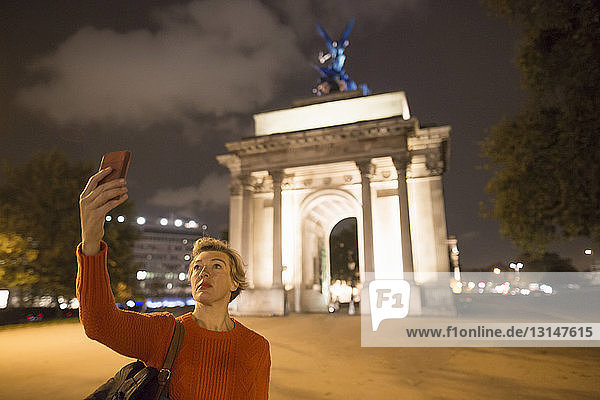 Ältere weibliche Touristin  die ein Smartphone-Selfie vom Wellington Arch bei Nacht macht  London  UK