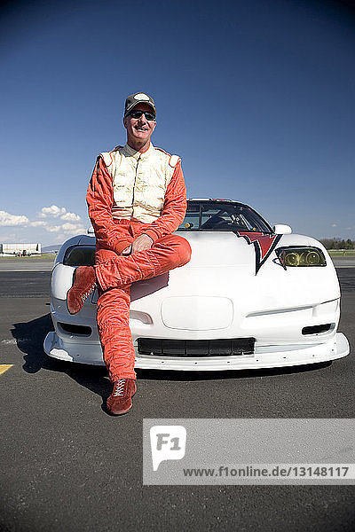 Portrait of mature male racing car driver leaning against racing car