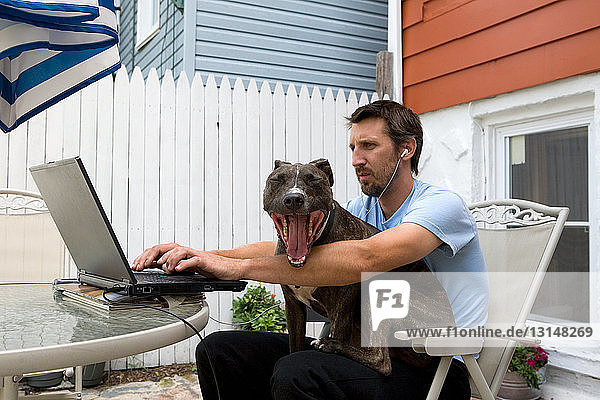 Man using laptop with dog sitting on lap
