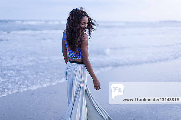 Junge Frau geht am Strand spazieren  schaut über die Schulter  lächelt