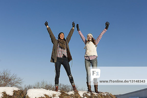 Zwei junge Frauen mit erhobenen Armen auf einer winterlichen Bergkuppe