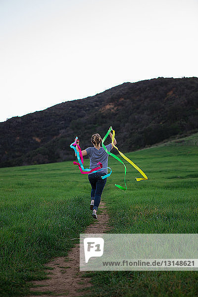 Rear view of young woman running on path holding up dance ribbons