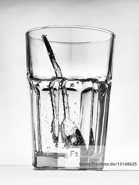 Still life of silver teaspoon inside glass of water