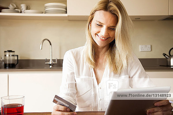 Mittlere erwachsene Frau in der Küche mit Kreditkarte und digitalem Tablet