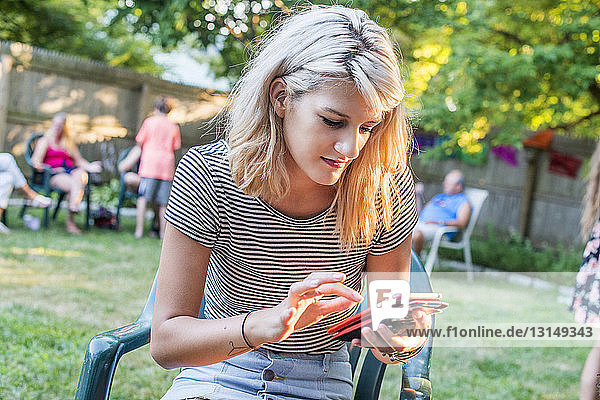 Junge Frau  die auf einer Party im Garten eine SMS auf ihrem Smartphone schreibt