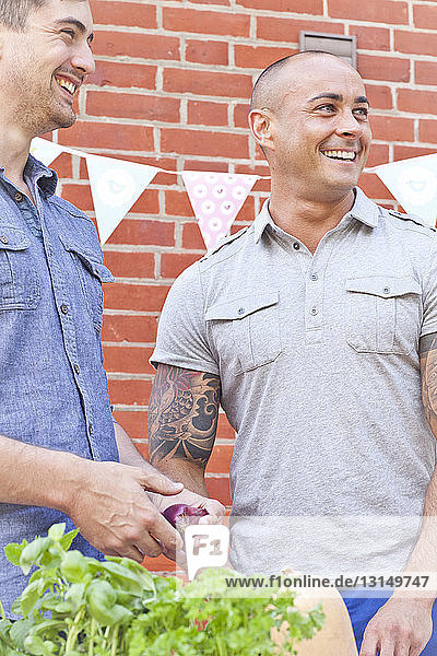 Zwei männliche Freunde lachen und bereiten Essen für ein Grillfest im Garten vor