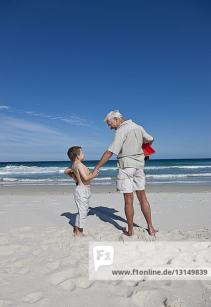 Mann hält die Hand seines Enkels am Strand