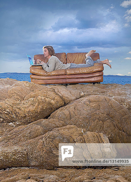 Mann mit Laptop auf Couch am Strand