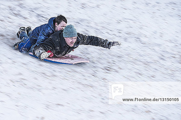 Vater und Sohn rodeln bergab im Schnee