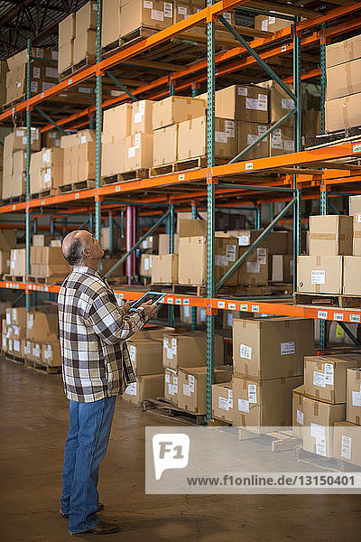 Warehouse worker with digital tablet looking at shelves of boxes