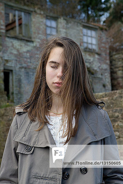 Teenage girl with eyes closed in front of derelict building