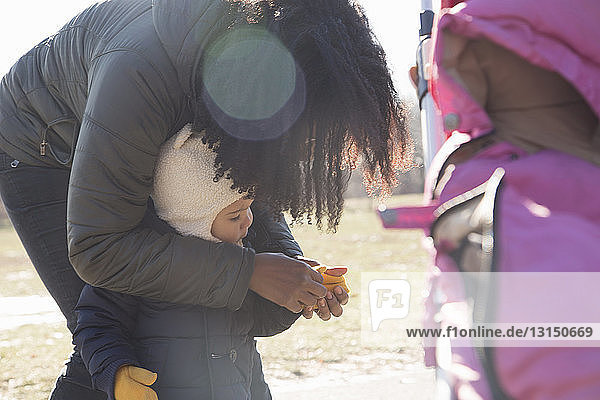 Mittlere erwachsene Frau zieht ihrer kleinen Tochter im Park Handschuhe an