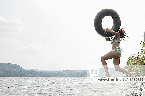 Junge Frau springt mit aufblasbarem Ring in den See