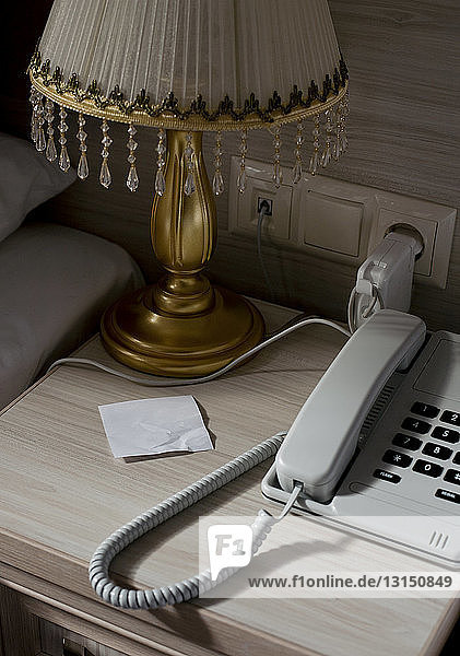 Festnetztelefon und leerer Zettel auf dem Nachttisch im Hotelzimmer