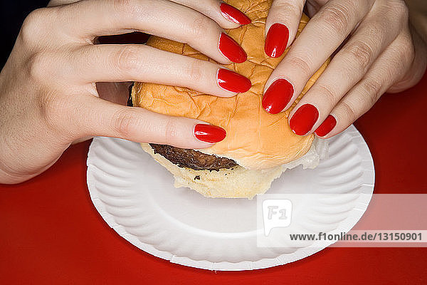 Frau mit roten Fingernägeln hält Burger