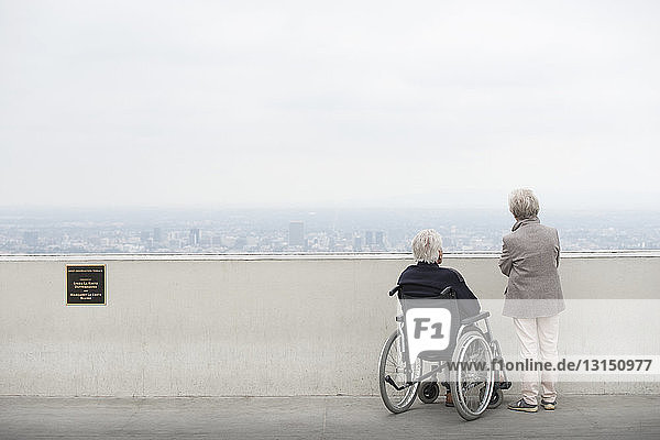 Rückansicht eines älteren Mannes im Rollstuhl und seiner Frau mit Blick auf die Stadt vom Aussichtsbalkon  Observatorium  Griffith Park  Los Angeles  Kalifornien  USA