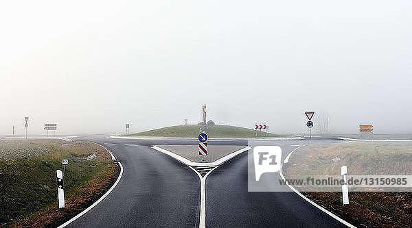 Kreisverkehr und Straße mit Schildern im Nebel