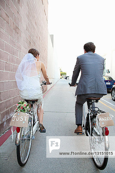 Junges  frisch verheiratetes Paar auf dem Fahrrad entlang der Straße  Rückansicht