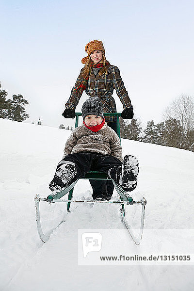 Young woman pushing boy on sled