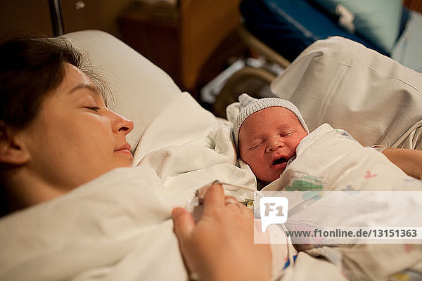Mother holding newborn baby boy in hospital bed
