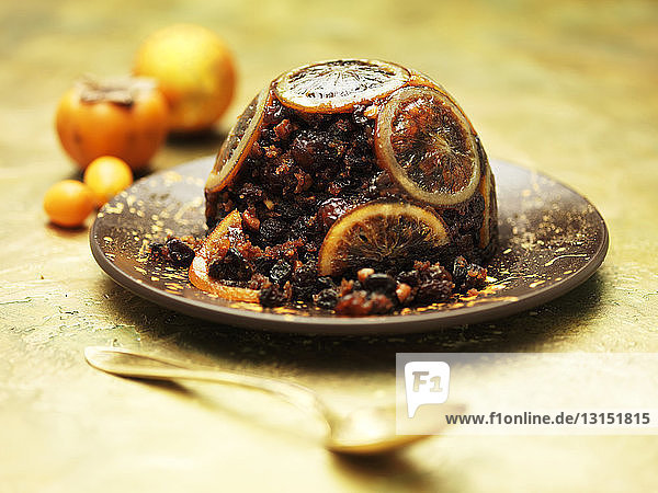 Orange topped Christmas pudding on brown ceramic plate