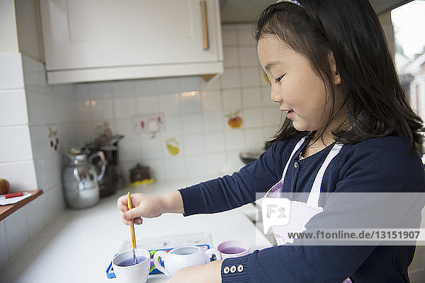 Junges Mädchen taucht Pinsel in Wasserschale in der Küche