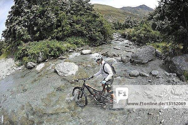 Frau schiebt Mountainbike durch Wasser  Neuseeland