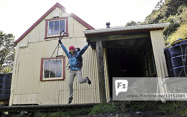 Wanderin springt mitten in der Luft vor einem Haus  Tararua Ridge  Neuseeland