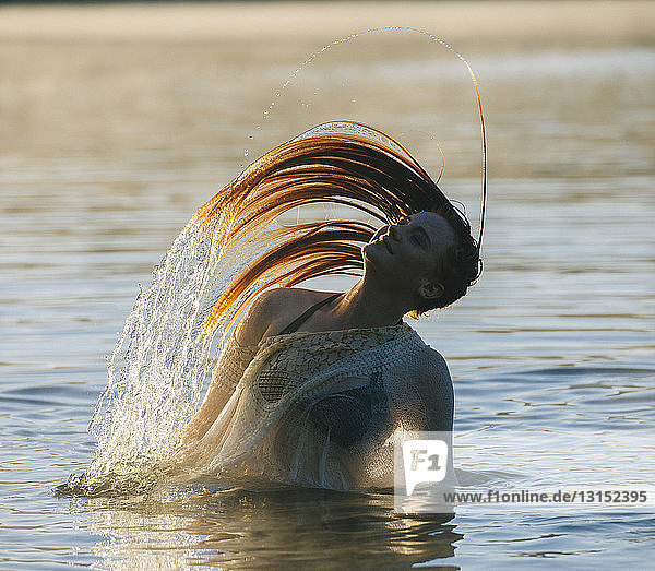 Junge Frau mit Bikinioberteil im Wasser  die ihr nasses Haar lächelnd zurückwirft