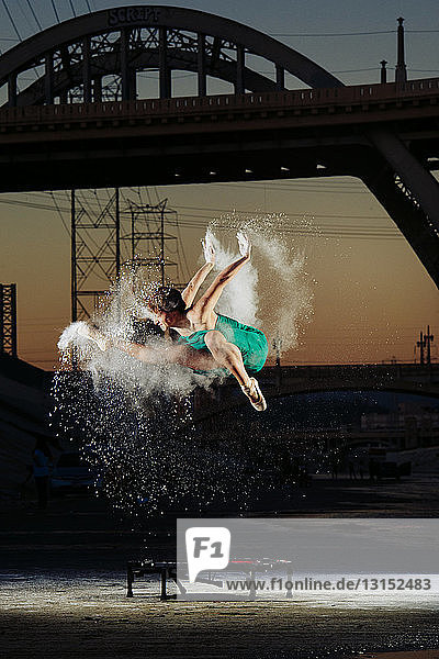 Eine Balletttänzerin springt  während sie eine Pulverexplosion über einem Trampolin bei Sonnenuntergang auslöst  Los Angeles  USA