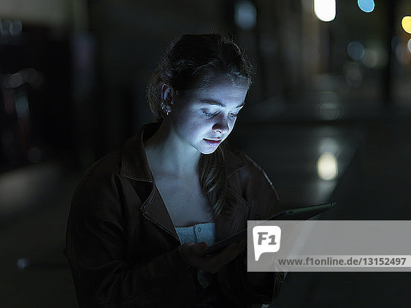 Junge Frau  die ein digitales Tablet benutzt  im Freien  bei Nacht  Gesicht beleuchtet