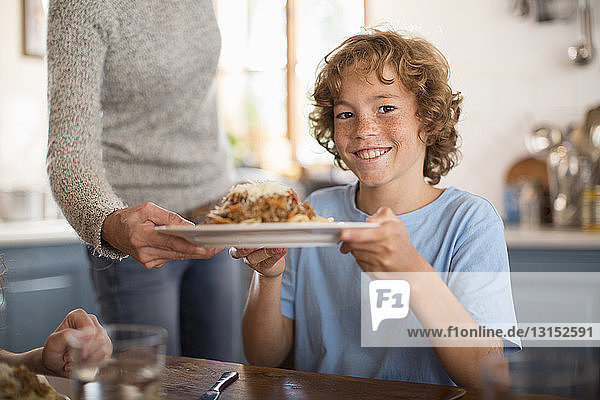 Mother serving spaghetti to children at dining table
