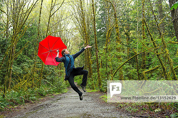 Springende Frau im Wald mit rotem Regenschirm