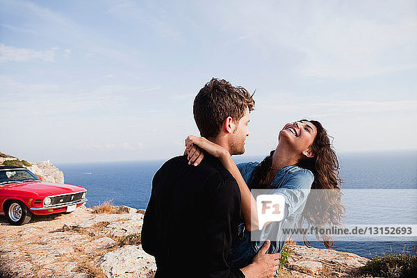 couple standing at cliff in front of car