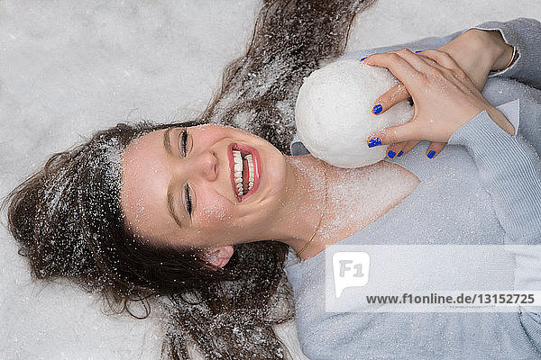 Lachende Frau liegt im Schnee und hält einen Ball