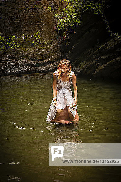 Mittlere erwachsene Frau in weißem Kleid sitzt auf den Schultern eines Mannes im Wasser und lacht