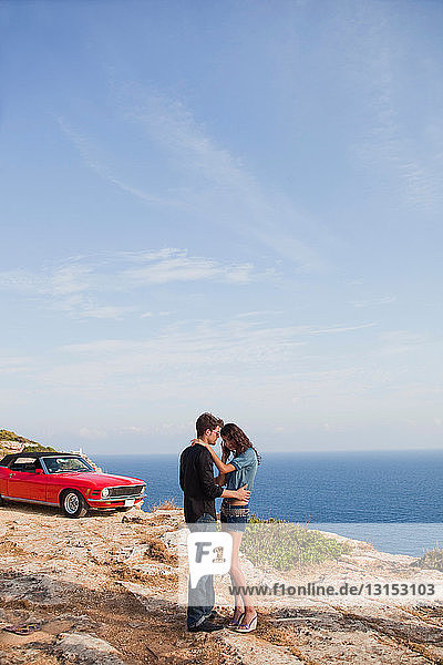 couple standing at cliff in front of car