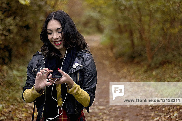 Young woman in park  listening to music using earphones