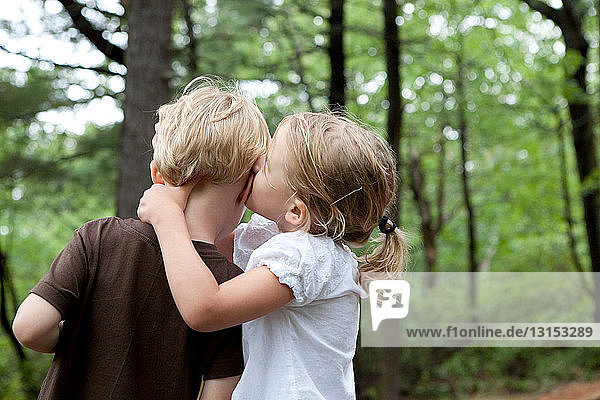 Mädchen flüstert ihrem Freund im Wald etwas zu