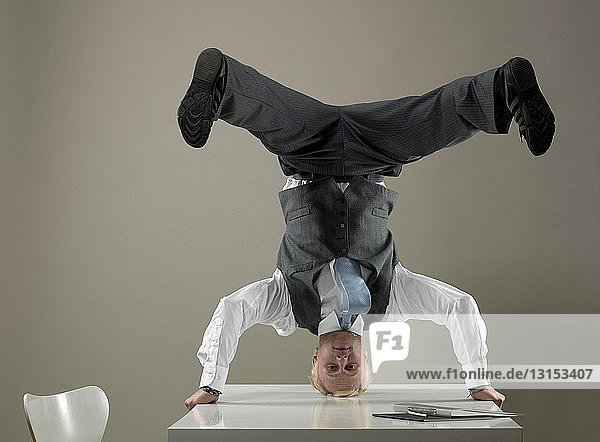 Business man standing on head on table