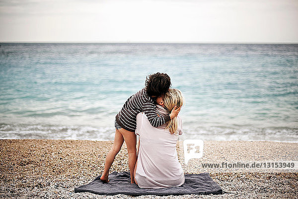 Junge  der seine Mutter am Strand umarmt  Rückansicht