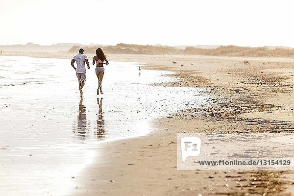 Couple running along beach  rear view