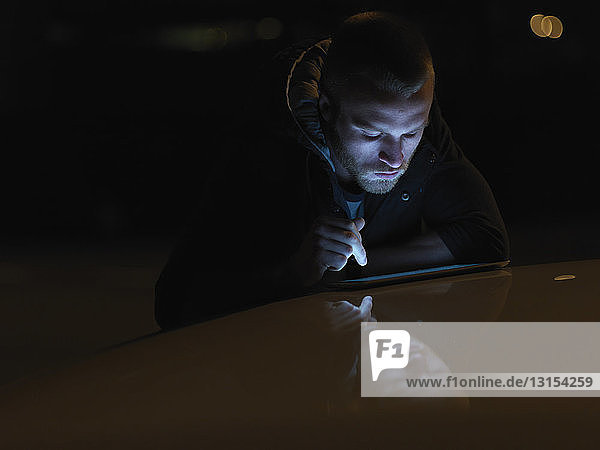 Junger Mann mit digitalem Tablet  im Freien  nachts  Gesicht beleuchtet