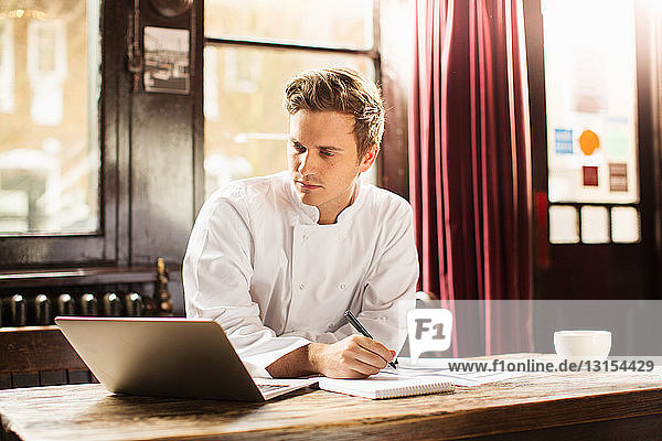 Young man wearing chef uniform using laptop