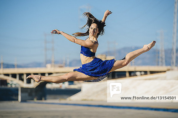 Seitenansicht einer jungen Frau  die in der Luft einen Spagat macht und lächelnd in die Kamera schaut  Los Angeles  Kalifornien  USA