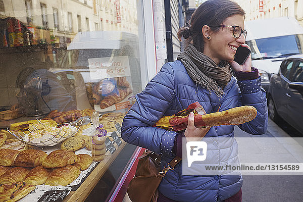 Mittlere erwachsene Frau vor einer Bäckerei in der Stadt beim Chatten mit dem Smartphone