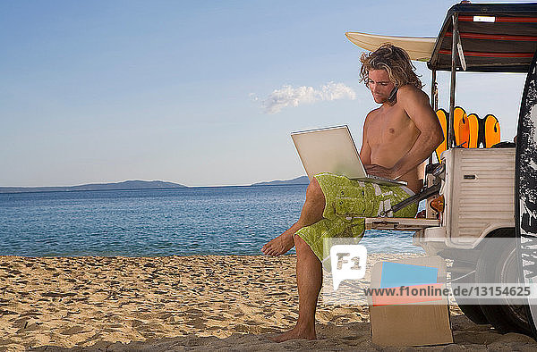 Mann am Strand Jeep mit Laptop  Telefon